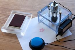 The stamper (right), shown with stamp pad. Pressing the blue accessibility switch activates the stamper.